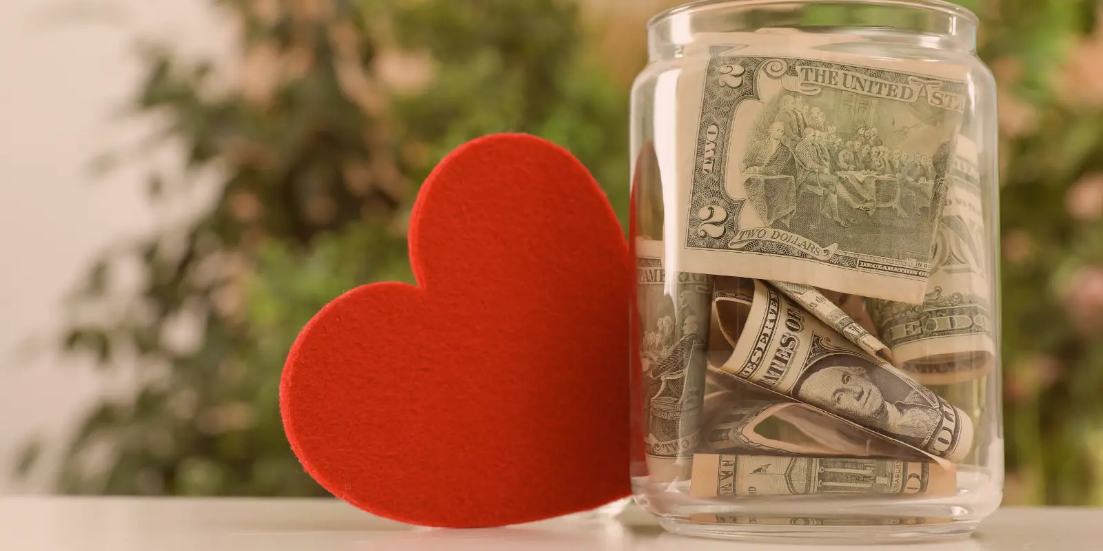 Jar with cash donations and a felt heart symbolizing community giving – donate to support local events and improvements.